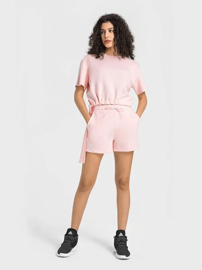 Woman wearing a pink sports short sleeves crop T-shirt with adjustable hem and matching shorts, ideal for fitness activities.